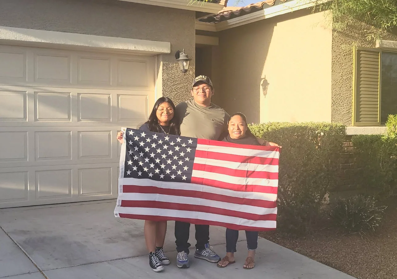 A family of three holding the American flag in the driveway of their new home.
