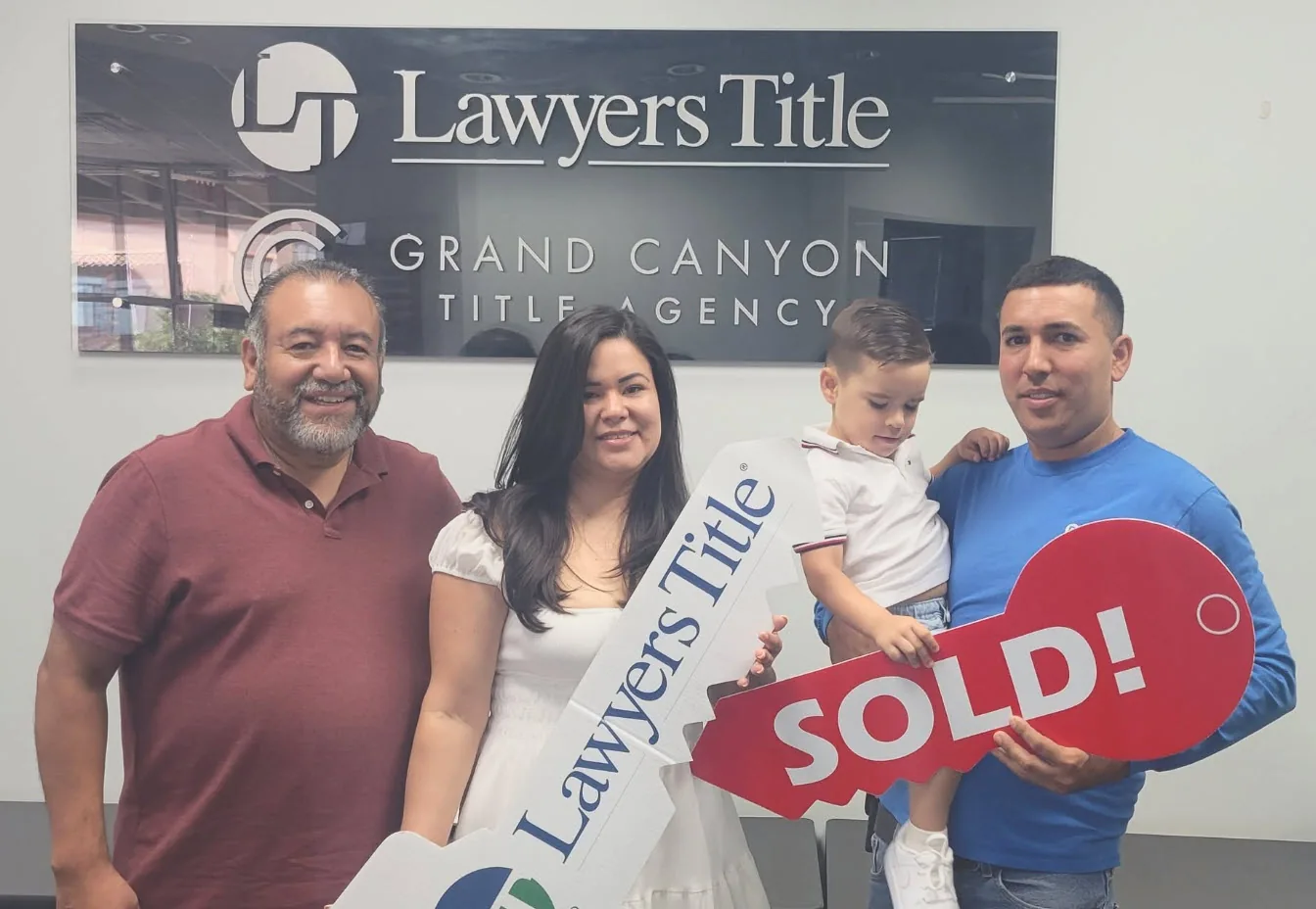 A family holding a big red SOLD key at the title agency on closing day.